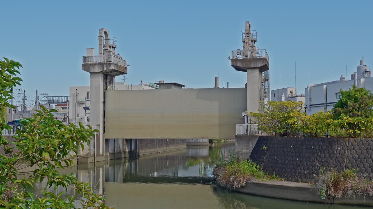 A straight-on view of the Old Ayase River Drainage Pump Station under a clear blue sky, framed by green foliage