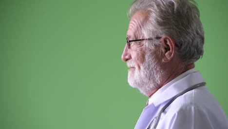 handsome senior bearded man doctor against green background