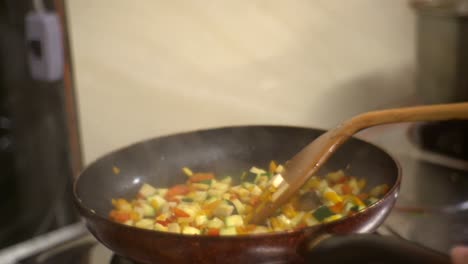 freshly chopped vegetables gently fried in flat frying pan while mixed with wooden spatula, filmed as close up