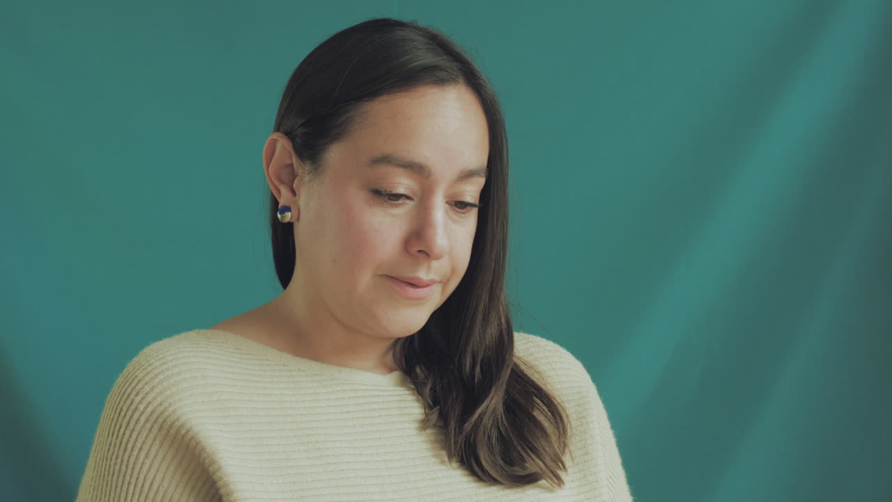 Medium shot of a young woman in focus on a professional recording set, with a solid turquoise background.
