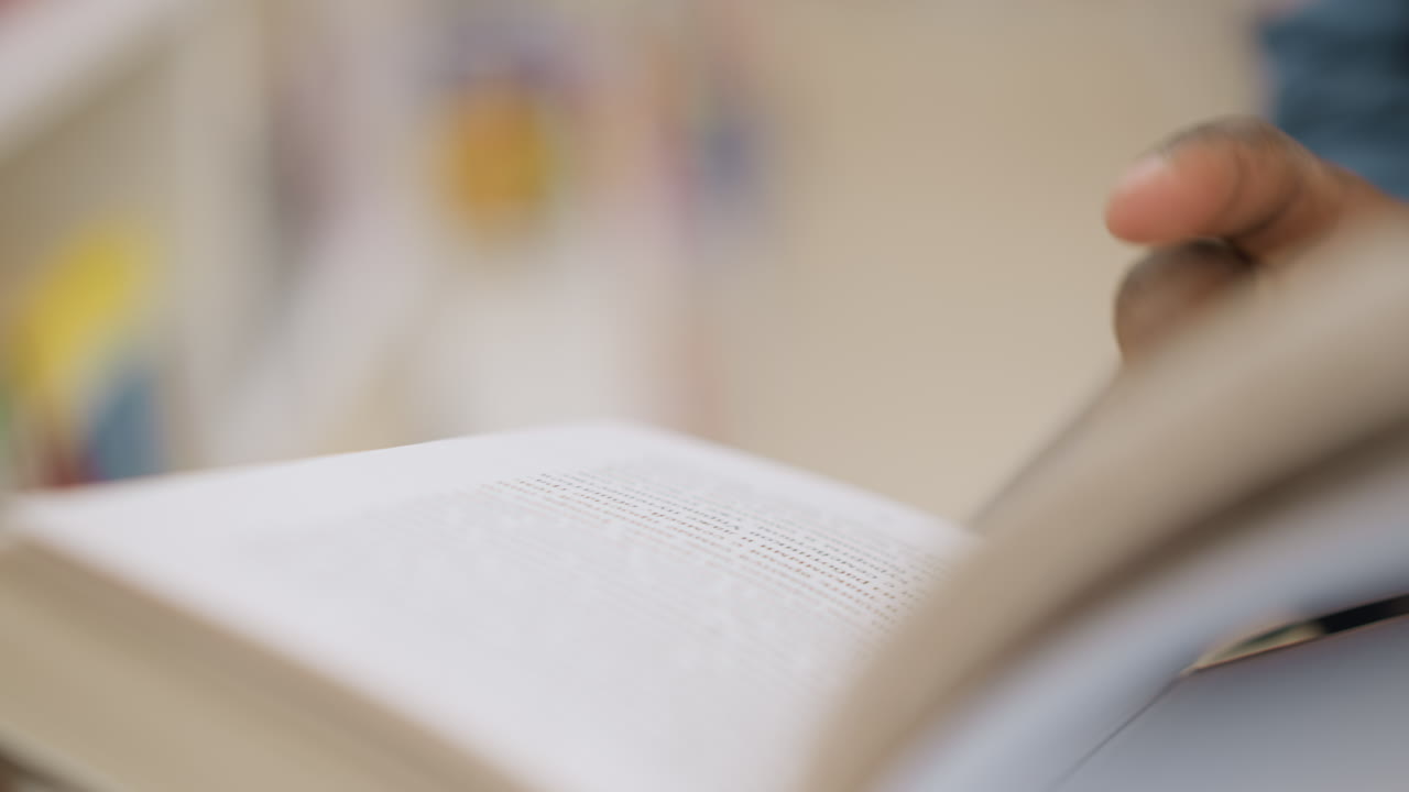 Close-up of hand flipping through book, fingers gently touching pages, focused on reading in soft ambient lighting with blurred background, capturing calm and intimate reading experience