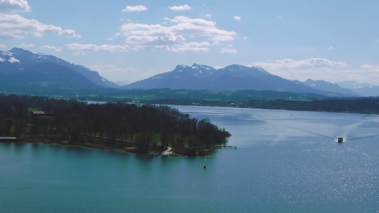 vista aérea escénica sobre el famoso lago chiemsee de baviera con su isla del castillo herrenchiemsee y un ferry en el campo rural con un hermoso cielo azul y las montañas de los alpes en el fondo