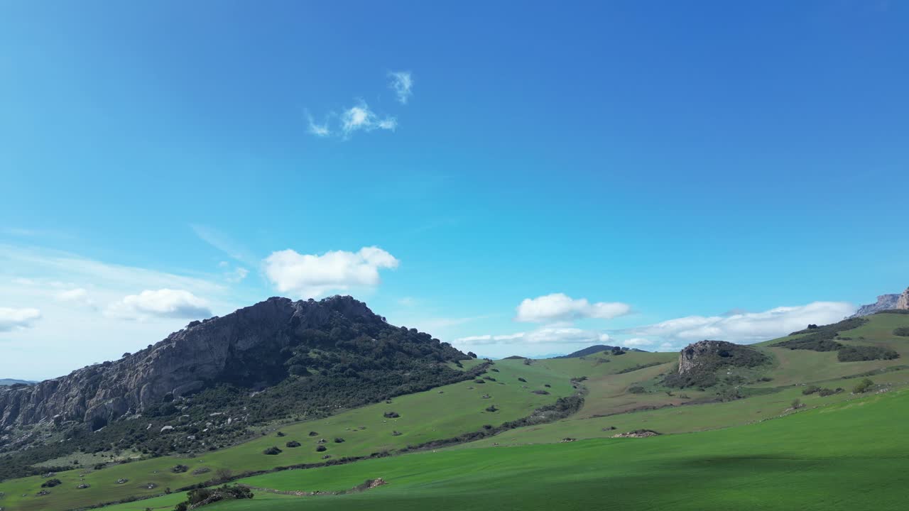 흰 구름이 있는 푸른 하늘을 배경으로 멋진 산이 있는 푸른 초원 위로 무인 항공기로 비행
