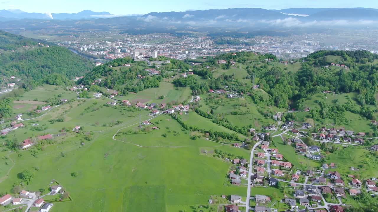 Mountain range green landscape with towns and single buildings in the valley connected by winding roads on a sunny day. Aerial drone shot. Kočevje - Slovenia