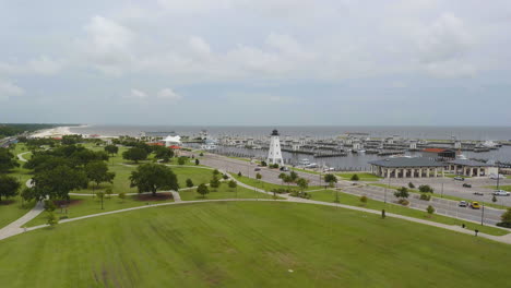 Aerial-view-of-a-lighthouse-on-the-edge-of-a-boat-dock-at-a-park-on-the-edge-of-the-ocean