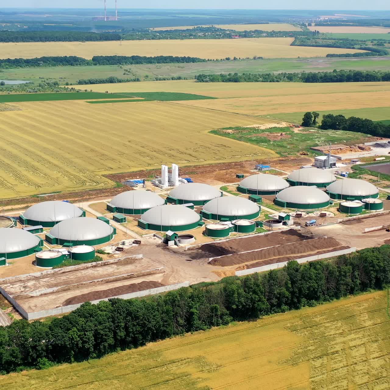 Innovative plant on yellow field. Biogas plant and storage tanks. Construction of biogas power plant in nature. Aerial view. Camera moving down