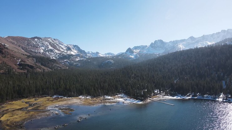 Drone che vola sopra un lago alpino verso montagne innevate a Mammoth Lakes.