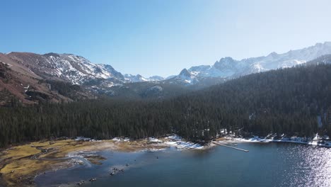 drone flying over alpine lake towards snowy mountains in mammoth lakes