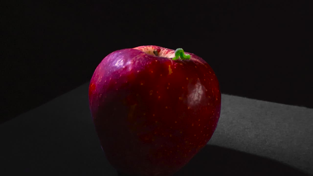 Tiny green inchworm crawling on the surface of a fresh red apple, a conceptual representation of nature's simple processes, healthy organic food, and the cycle of life on a dark background