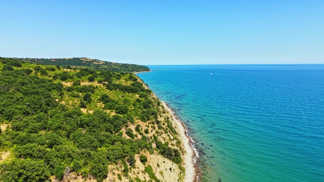 Güneşli bir günde, berrak bir gökyüzünün yakınında su ve karayla bir sahil şeridinin manzaralı görünümü.