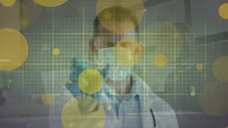 Animation-of-floating-yellow-dots-over-caucasian-male-doctor-in-face-mask