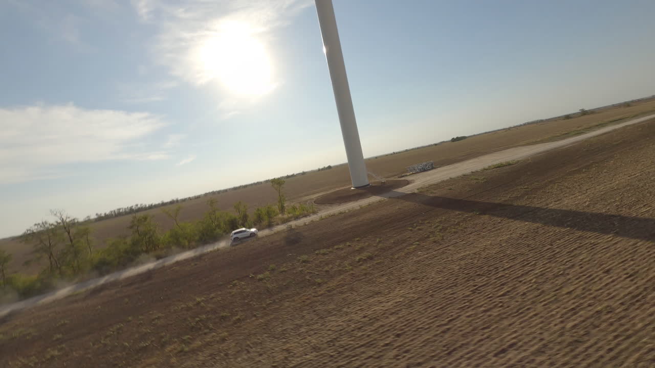 White SUV driving on a rural road near a wind turbine