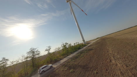 White SUV driving on a rural road near a wind turbine