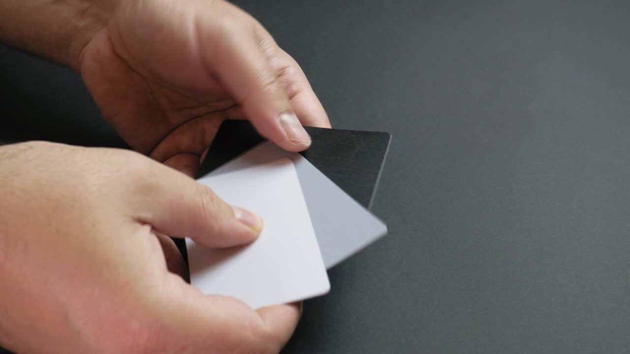 Hands of a man showing white, 18 percent gray and black color grading white balance cards. Close up