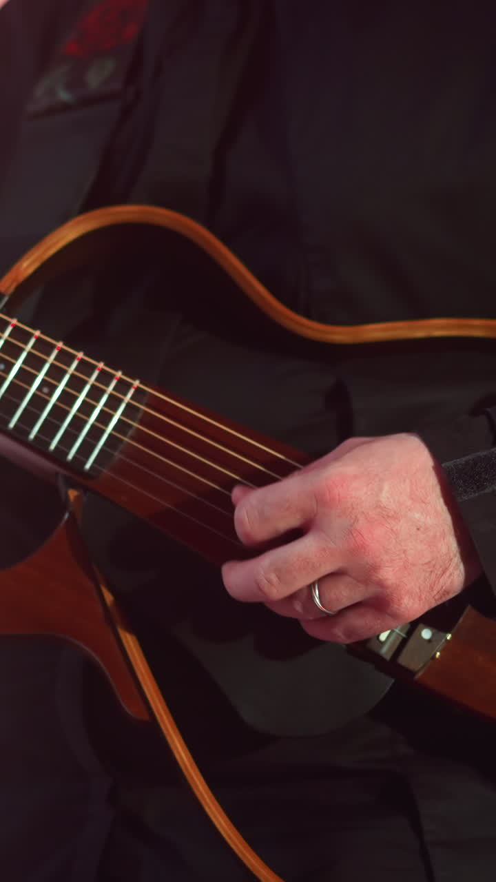 la mano enfocada del guitarrista tocando una guitarra roja contra un fondo gris suavemente borroso, con otra guitarra débilmente visible en el fondo