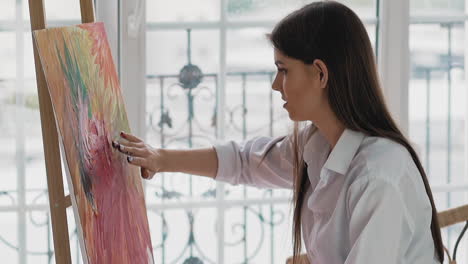 woman artist applies paint on canvas by fingers in studio