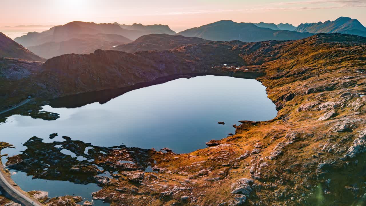 bumannsvatnet: un pequeño lago, el agua como un espejo refleja cielos despejados arriba, el cielo es brumoso y de color rosa anaranjado, lo que le da una sensación etérea de ensueño a la imagen