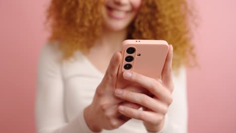 crop woman using smartphone in pink studio