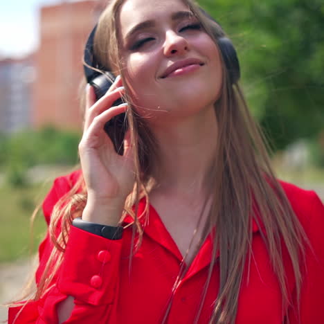 attractive woman listening to music outdoors. young female in red dress with headphones enjoys music in the city street in summer.
