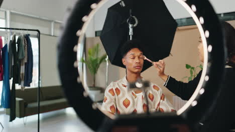 makeup artist applying makeup to a man in a studio