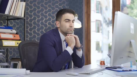 Thoughtful-Looking-Office-Worker-Man-Looking-At-Computer-While-Sitting-At-Desk.
