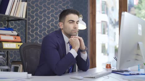 thoughtful looking office worker man looking at computer while sitting at desk.