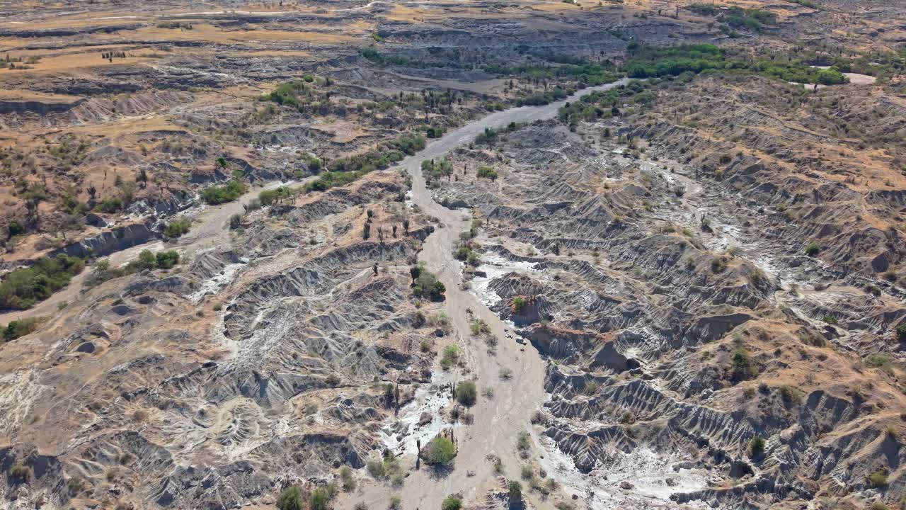 Un drone aereo segue due grandi letti di fiume prosciugati attraverso canyon desertici grigi di Tatacoa, simili a un terreno, convergono in un unico vasto canale rivelando l'erosione su larga scala e la drammatica geologia arida dall'alto