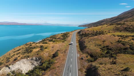 aerial follow view of a van driving next to lake pukaki in summer time in new zealand