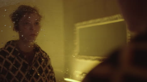 woman looking at reflection in wet mirror