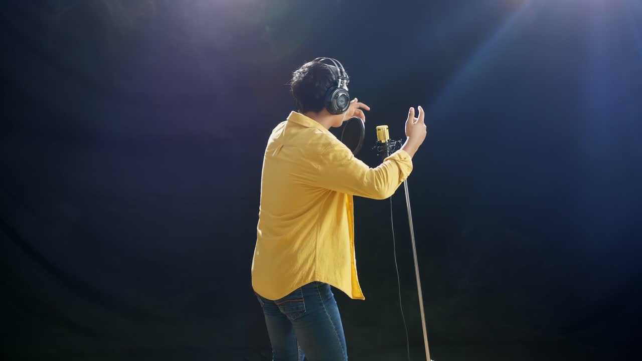 vista trasera de un niño con auriculares golpeando en un micrófono condensador en el fondo negro de humo blanco