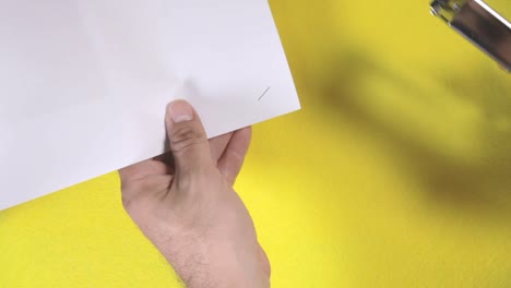 a silver metallic stapler fastens a collection of printed papers, forming an angled crimped junction