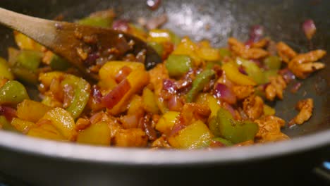 panning across mexican style fajita mix with chicken, peppers, onions with spicy seasoning and wooden spoon resting in pan after cooking on high heat.