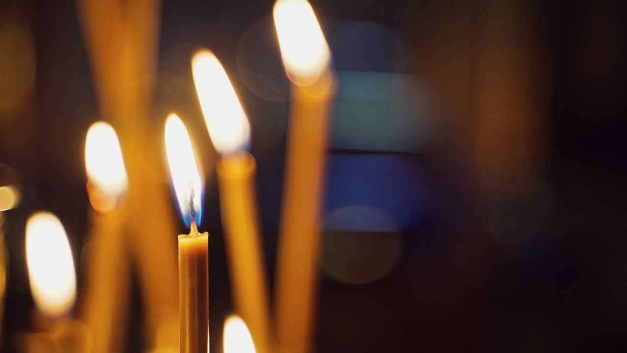 Bright candles are glowing on the blurred background. Church candles burning in the night temple. Candles flame.