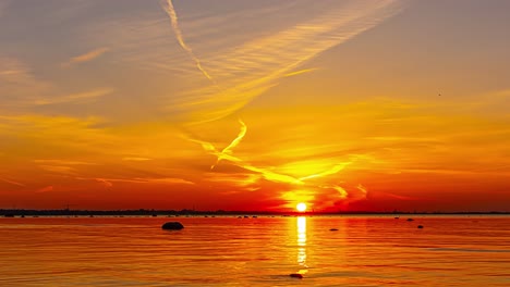 Lebendiger-Zeitraffer-Sonnenuntergang-über-Der-Ostsee-In-Tallinn,-Estland,-Der-Einen-Warmen-Glanz-Auf-Das-Wasser-Und-Die-Skyline-Der-Stadt-Wirft,-Mit-Silhouetten-Verankerter-Boote,-Während-Wolkenstreifen-Darüber-Ziehen