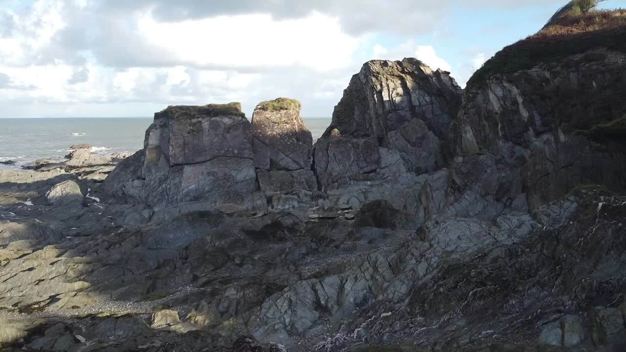 공중 드론은 바위가 많은 해변 위를 빠르게 날고 바다로 나가는 암석 사이를 통과합니다 - 리 베이, 비치, 일프라콤, 데본