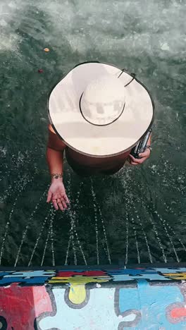 woman in a hat enjoying a water fountain