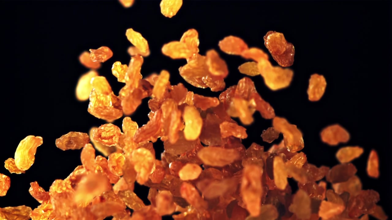 Goldene Rosinen fallen und häufen sich auf schwarzem Hintergrund in Zeitlupe