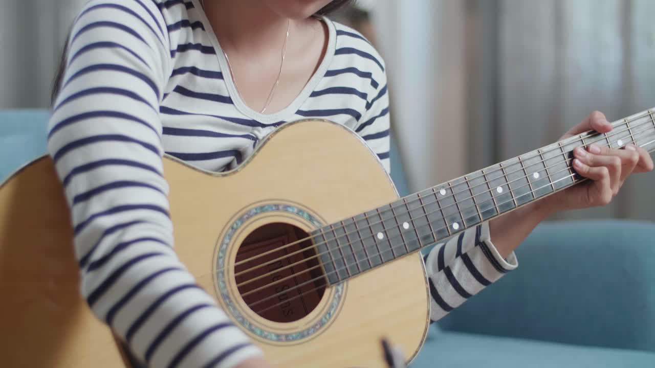 집에서 종이에 음악을 작곡하기 전에 기타를 들고 있는 아시아 여성 작곡가의 클로즈업