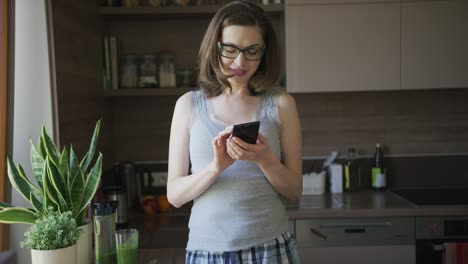 Mujer-Atractiva-Con-Smartphone-De-Pie-En-La-Cocina