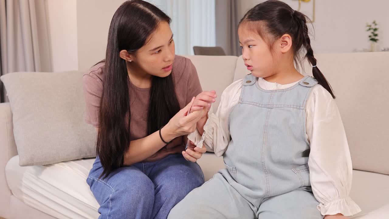 A mother tends to her daughter's finger injury on a cozy living room sofa, fostering a caring and nurturing atmosphere