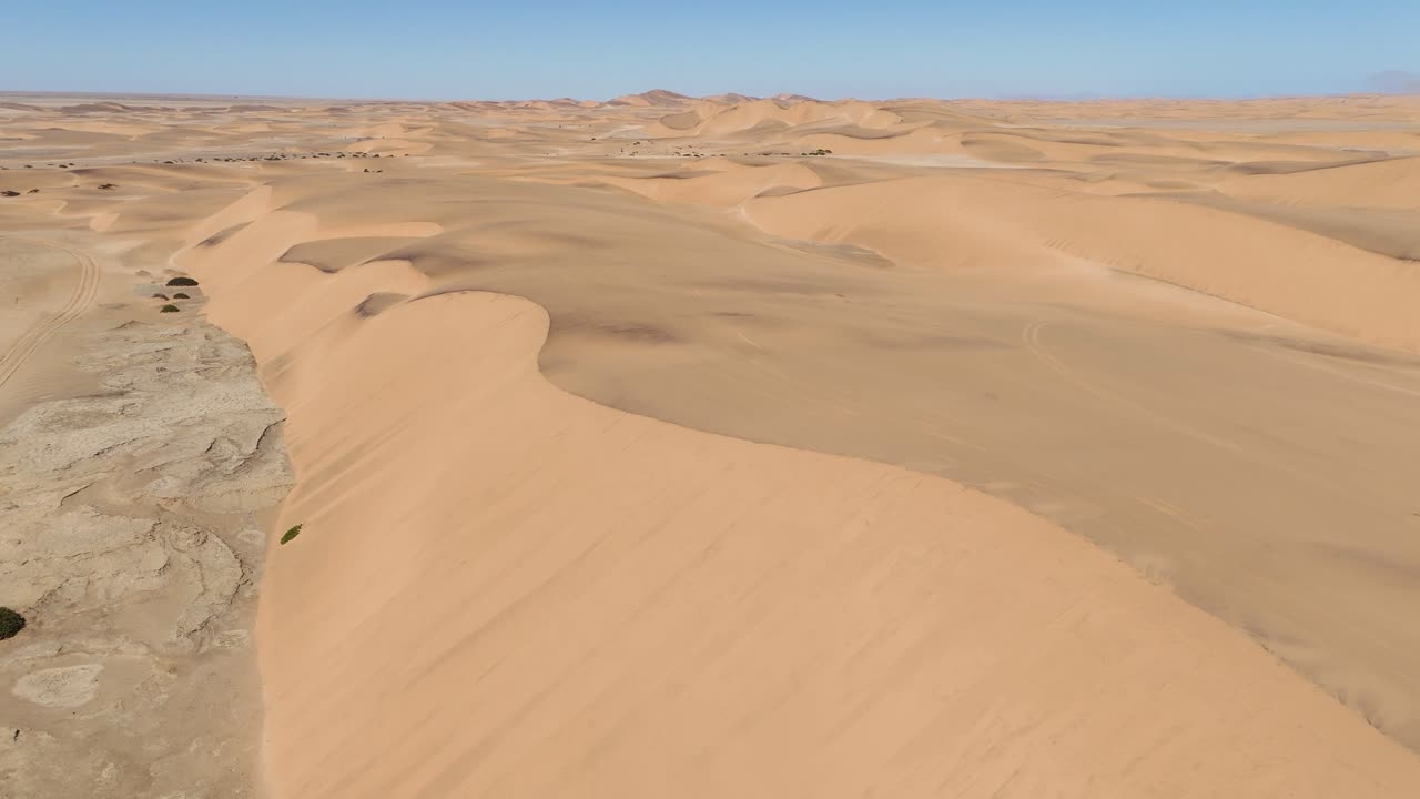 High-altitude aerial shot of the Namib Desert coastline near Swakopmund, showing endless dunes fading into the Atlantic horizon