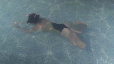 una hermosa joven nada bajo el agua dentro de una piscina