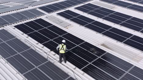 trabajador masculino limpiando el panel solar en el techo de un gran almacén usando un motor de cepillo giratorio eléctrico con cabezas dobles - disparo de drones de retroceso