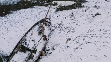 Aerial-shot-of-an-abandoned-boat-on-the-shore,-frozen-and-snowy-ground-surface