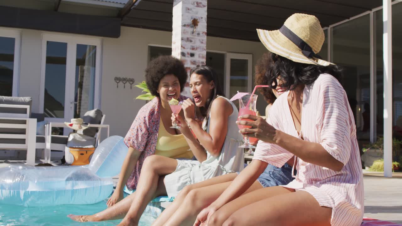 Happy diverse female friends talking and smiling at swimming pool party