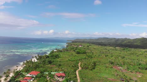 Drone-flying-down-tropical-island-covered-in-palm-trees,-by-the-sea