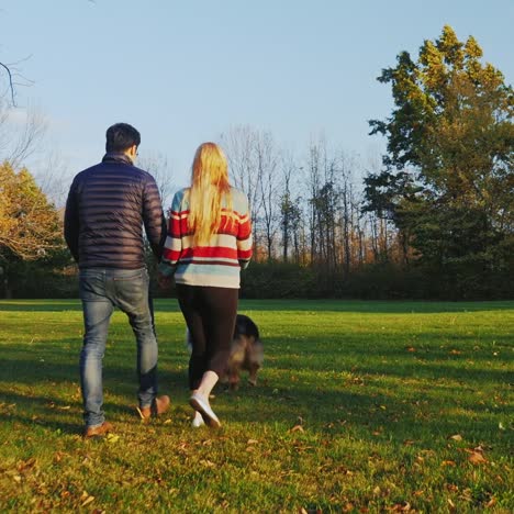 Junges-Sorgloses-Paar,-Das-Mit-Einem-Hund-Im-Park-Spazieren-Geht-1