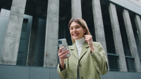 attractive blond woman celebrate online win great news, feel amazed outdoor.closeup of girl reading good news in smartphone makes yes hand gesture