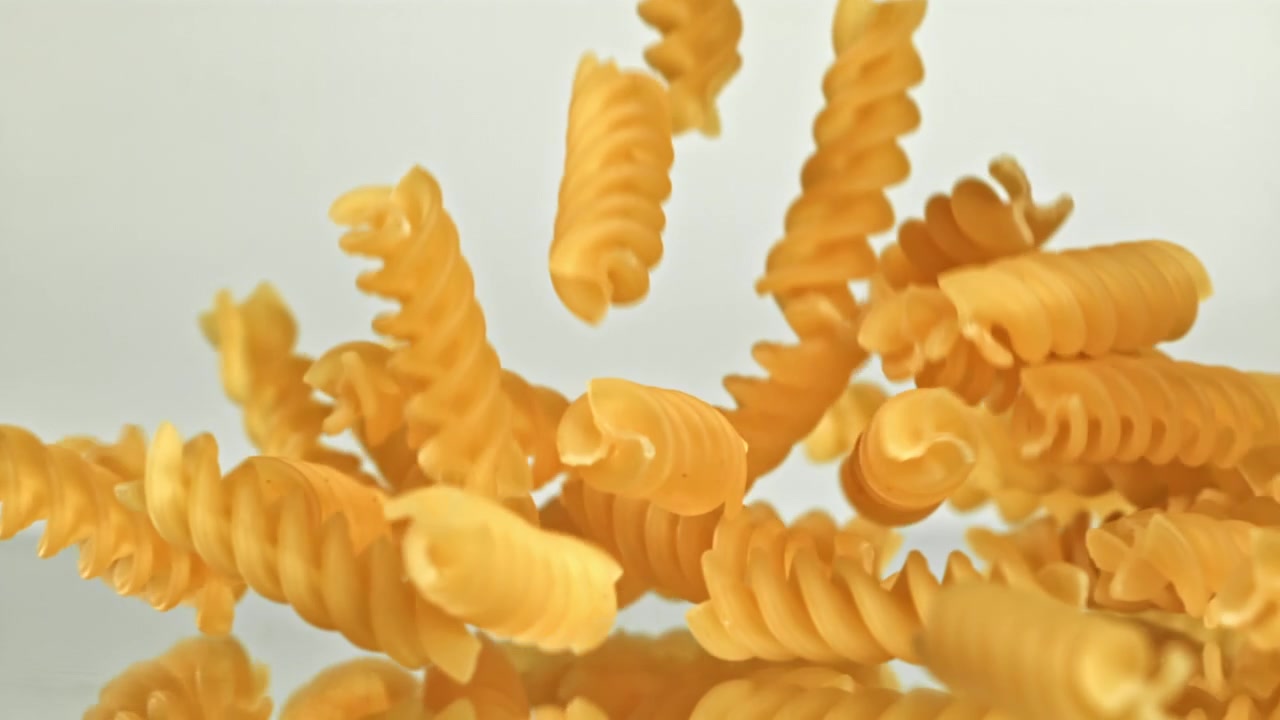 Fusilli crudi che cadono al rallentatore su una superficie riflettente