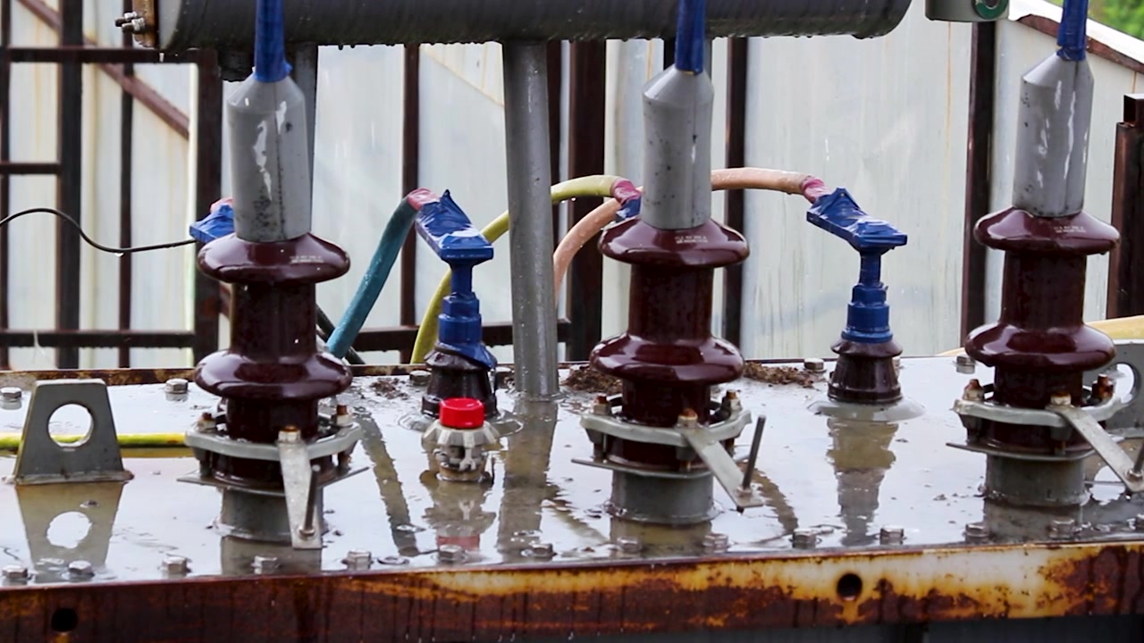 Close-up of rain falling on a high voltage electrical transformerd insulators. Ideal for energy, power grid, infrastructure, utility, weatherd industrial safety projects.